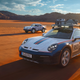 The 2023 Porsche 911 Dakar drives in the desert next to a 1984 Carrera 4WD race car.